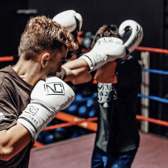 Two male boxers training with white NC Fitness boxing gloves in a gym ring.