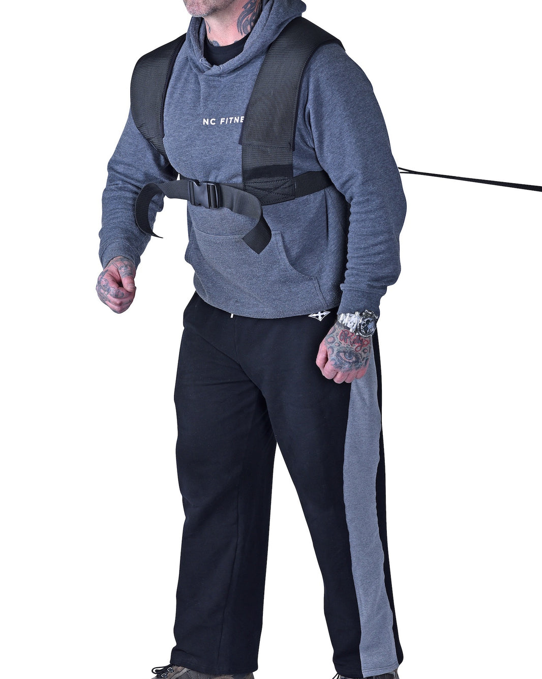 Person wearing a gray hoodie and black pants with a harness on a white background