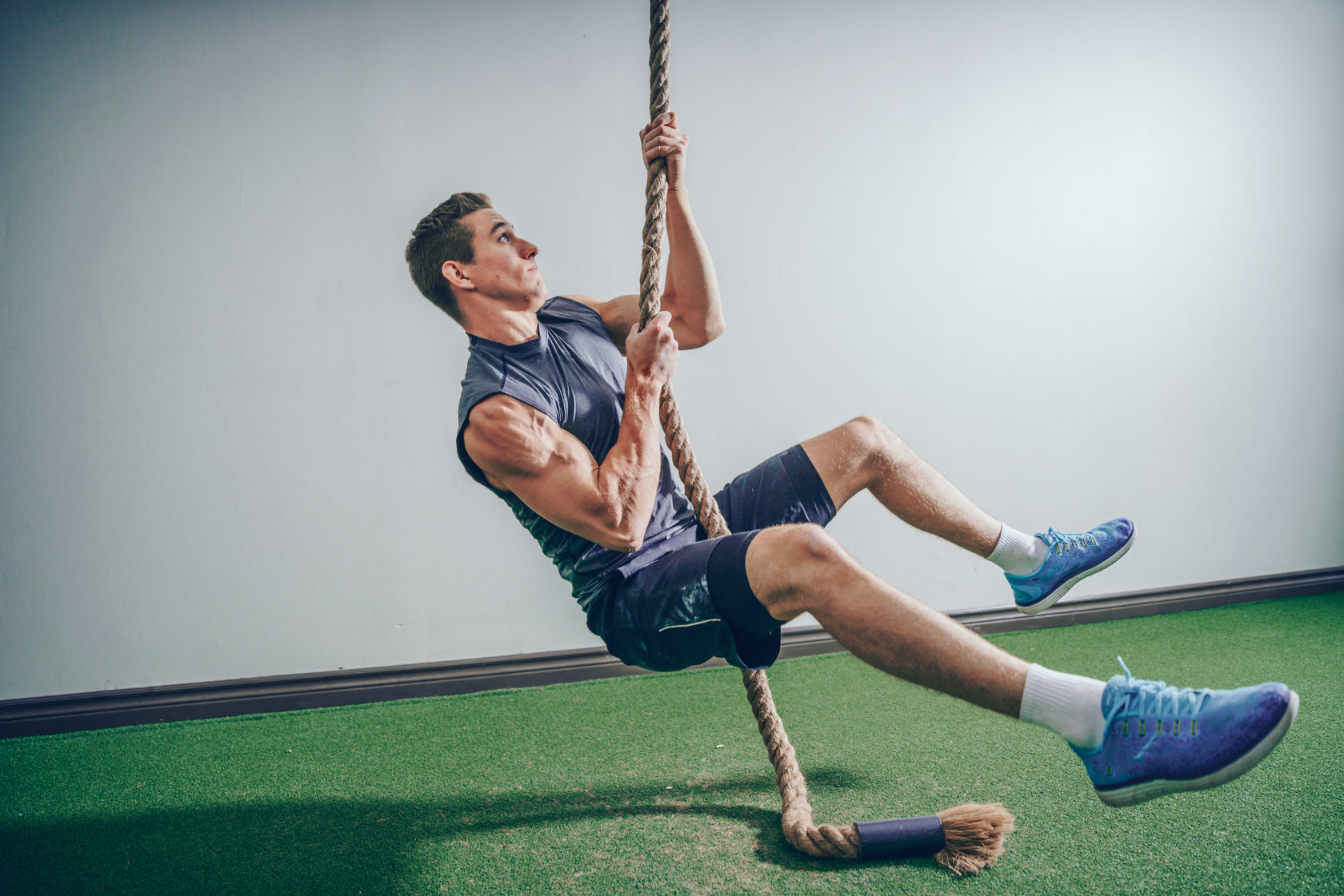 Man performing a rope climb workout in a commercial gym setting.