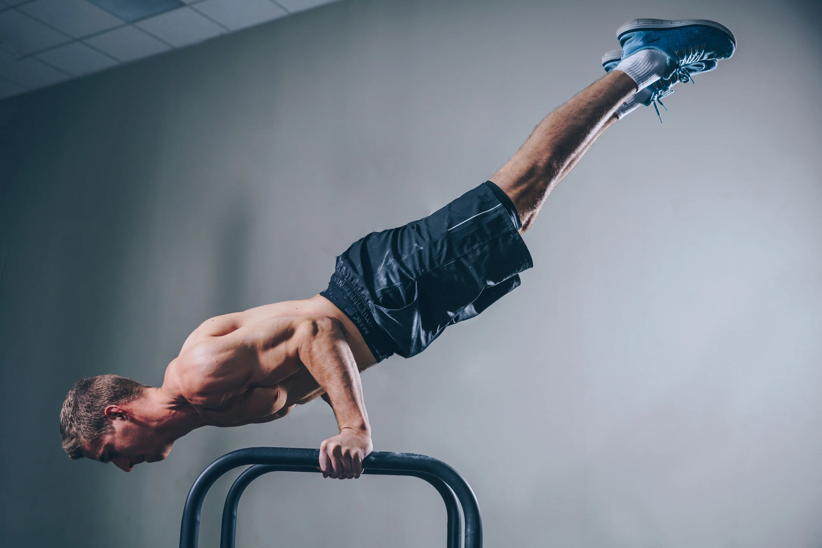 Muscular man performing a handstand on parallel bars in a gym.