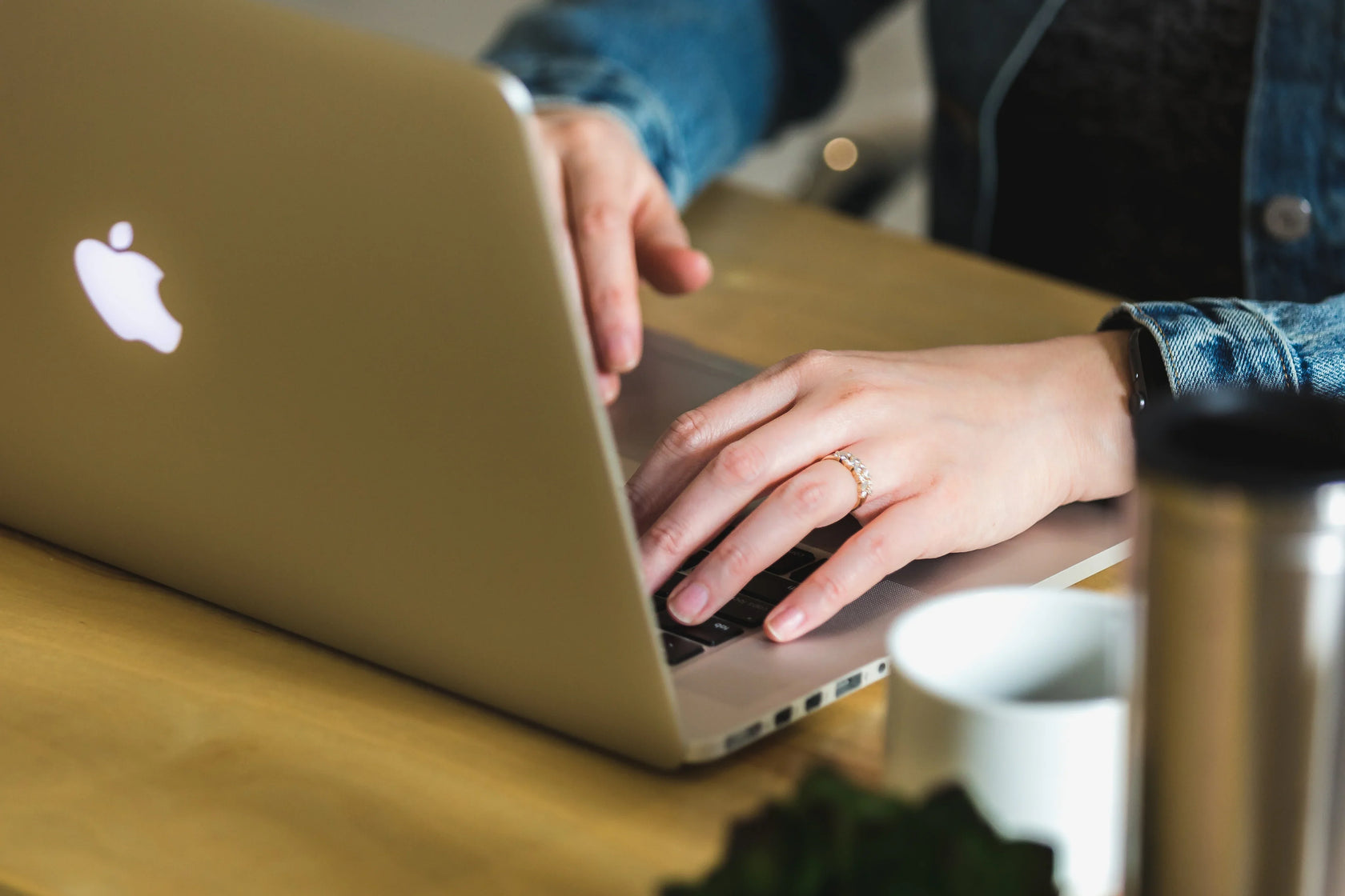Person typing on a silver laptop at a wooden desk with a coffee mug nearby.