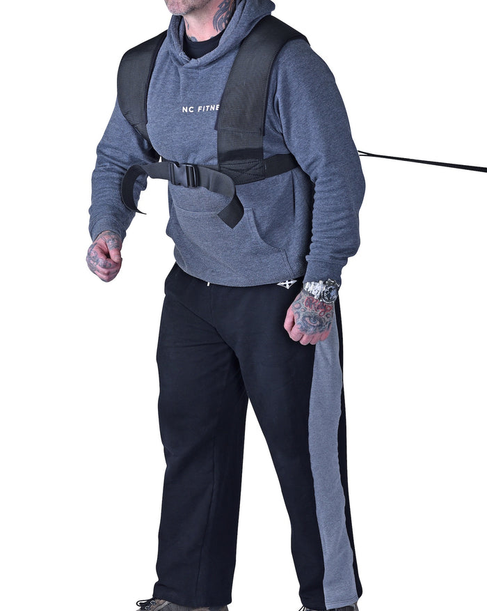 Person wearing a gray hoodie and black pants with a harness on a white background