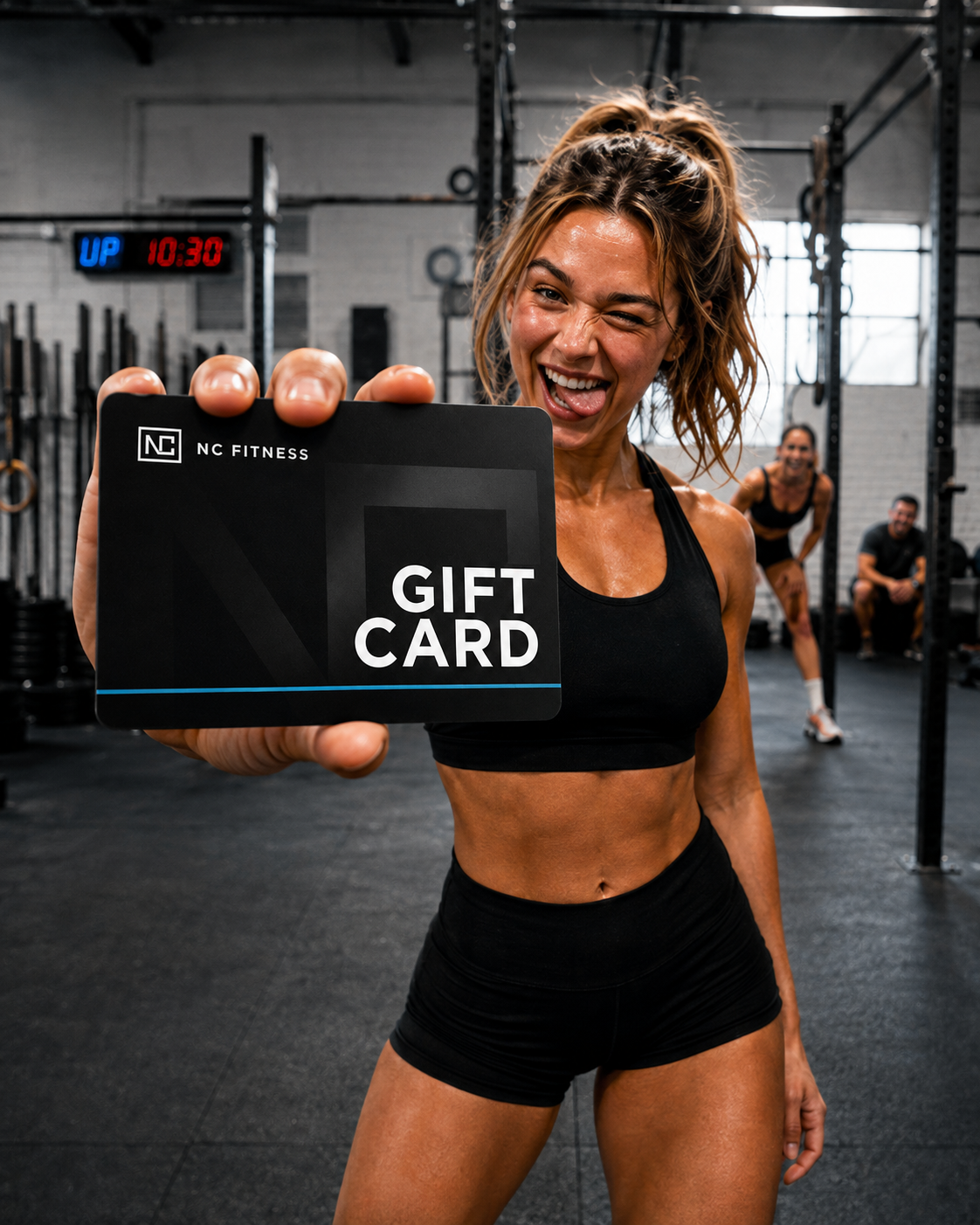 A woman in a gym holding up a black NC Fitness gift card with white text. The background shows a gym interior with other people and exercise equipment.
