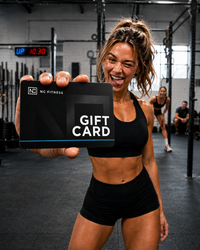 A woman in a gym holding up a black NC Fitness gift card with white text. The background shows a gym interior with other people and exercise equipment.